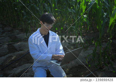 Agricultural researcher analyzing corn field data with laptop Agricultural researcher analyzing corn field data with laptop 139898428