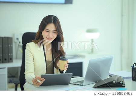 Businesswoman reviewing data on tablet with coffee, Professional woman holding coffee while analyzing digital report on tablet 139898468