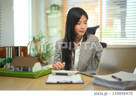 Real estate professional calculating property costs at desk, businesswoman calculating housing expenses. 139898470
