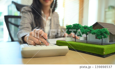 Real estate professional calculating property costs at desk, Close up of businesswoman calculating housing expenses. Real estate professional calculating property costs at desk, Close up of businesswoman calculating housing expenses. 139898537