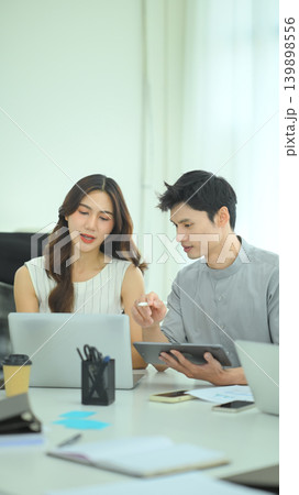 Business professionals comparing printed reports and digital statistics during office discussion, Colleagues reviewing financial charts on laptop and tablet Business professionals comparing printed reports and digital statistics during office discussion, Colleagues reviewing financial charts on laptop and tablet 139898556