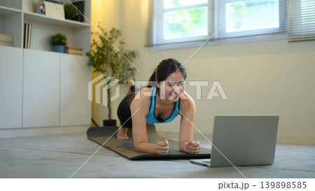 Woman doing plank workout while following laptop, home fitness and online training concept Woman doing plank workout while following laptop, home fitness and online training concept 139898585