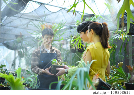 Gardener handing plant to happy couple in nursery Gardener handing plant to happy couple in nursery 139898635