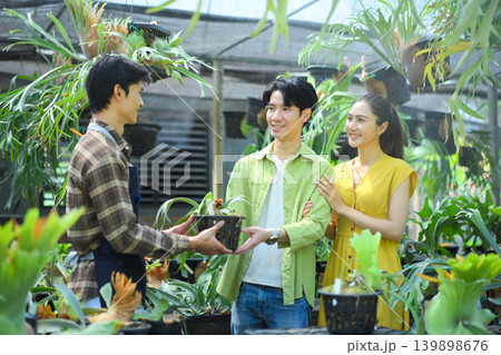 Gardener handing plant to happy couple in nursery Gardener handing plant to happy couple in nursery 139898676