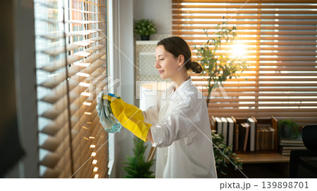 Woman Cleaning Window Blinds with Disinfectant Spray 139898701