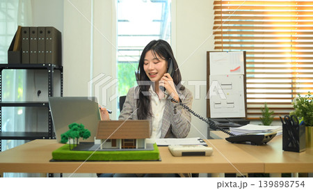 Real estate agent calculating property cost while talking on phone, woman discussing property details at desk Real estate agent calculating property cost while talking on phone, woman discussing property details at desk 139898754