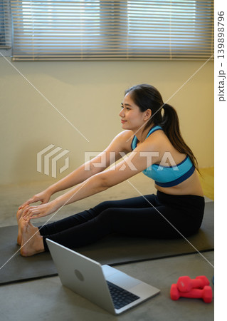 Woman stretching legs on yoga mat with laptop, home fitness and flexibility training concept Woman stretching legs on yoga mat with laptop, home fitness and flexibility training concept 139898796