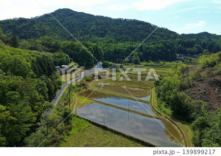 新緑の里山と水田が広がる農村風景の空撮写真 新緑の里山と水田が広がる農村風景の空撮写真 139899217