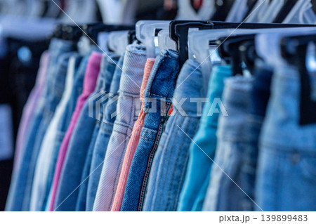 Close-up of various denim jeans hanging on a clothing rack in a retail shop. Close-up of various denim jeans hanging on a clothing rack in a retail shop. 139899483
