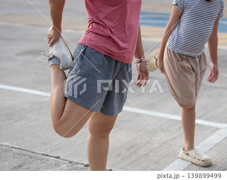 Close-up of a mother and daughter doing lunge stretching exercises together outdoors. Close-up of a mother and daughter doing lunge stretching exercises together outdoors. 139899499