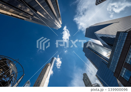 New york, usa august 19,2024. Urban architecture forms an upward perspective of modern glass towers and office buildings against a vibrant blue sky with clouds 139900096