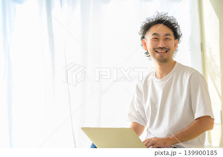自宅でノートパソコンを使う笑顔の日本人男性 自宅でノートパソコンを使う笑顔の日本人男性 139900185