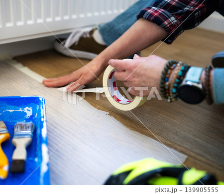 Girl Applying Painting Tape for Flooring Project Indoors Girl Applying Painting Tape for Flooring Project Indoors 139905555