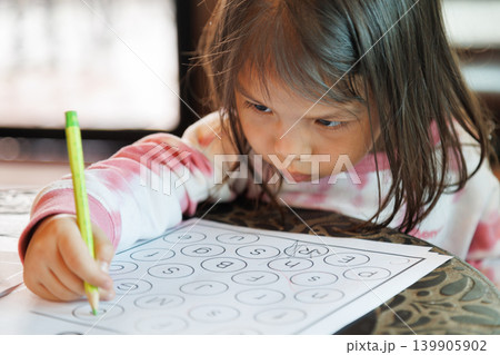portrait of cute little Asian girl holding a pencil and writing on paper worksheet. focused preschool child doing homework at home or school for early childhood education and development concept. portrait of cute little Asian girl holding a pencil and writing on paper worksheet. focused preschool child doing homework at home or school for early childhood education and development concept. 139905902