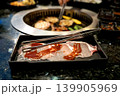 Fresh raw sliced pork with red marinade on a tray with metal tongs. Background shows a traditional yakiniku barbecue grill with meat cooking in a restaurant. 139905969