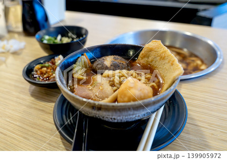 Delicious Japanese ramen bowl with noodles, shiitake mushroom, pork belly, and fish cake on a wooden table. Asian fusion cuisine served with side dishes and chopsticks in a modern restaurant. 139905972