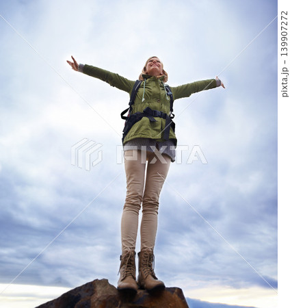 Woman, hiking and freedom on mountain top for travel, success and achievement or fresh air on cloudy sky. Young person in backpack and stretching arms for trekking, journey or adventure in low angle 139907272