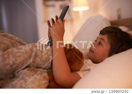 Boy, child and tablet in bedroom at night for typing, reading or online game with app in family home. Kid, bed and digital touchscreen for movie, cartoon and streaming subscription to relax in house Boy, child and tablet in bedroom at night for typing, reading or online game with app in family home. Kid, bed and digital touchscreen for movie, cartoon and streaming subscription to relax in house 139907292