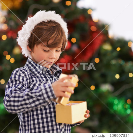 Happy, Christmas and boy child with gift for celebration or surprise at festive party at home. Smile, santa hat and cute young kid opening a present box for xmas event at modern house with decoration Happy, Christmas and boy child with gift for celebration or surprise at festive party at home. Smile, santa hat and cute young kid opening a present box for xmas event at modern house with decoration 139907834