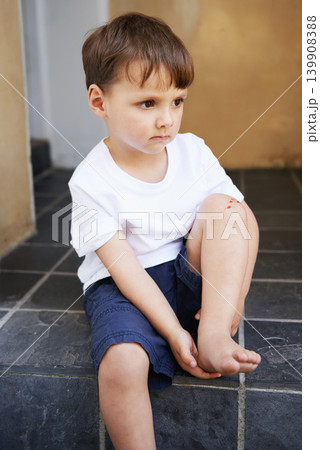 Little boy, sitting and injury on knee in home and accident, ache and with blood from cut. Young child, sad and holding hurt leg up with hand on foot, pain and sore on bruise with fear of trouble 139908388