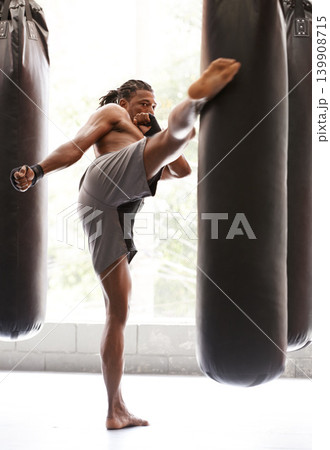 Man, kick boxing and bag with exercise, foot and combat for training with balance, power and precision in gym. African athlete, person or fighter with workout, fitness or strike for challenge in dojo Man, kick boxing and bag with exercise, foot and combat for training with balance, power and precision in gym. African athlete, person or fighter with workout, fitness or strike for challenge in dojo 139908715