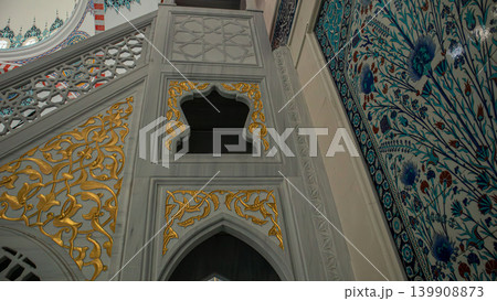 Inside the mosque, the wall features intricate floral tiles in Iznik style. The blue and red tulip designs add character to the sacred place. Visitors admire the craftsmanship and artistry. Inside the mosque, the wall features intricate floral tiles in Iznik style. The blue and red tulip designs add character to the sacred place. Visitors admire the craftsmanship and artistry. 139908873