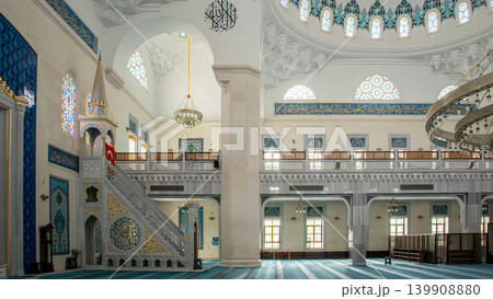 The mosque interior shows a marble minbar with golden accents. A Turkish flag is displayed against arched galleries. The space is designed for prayer and reflection. The mosque interior shows a marble minbar with golden accents. A Turkish flag is displayed against arched galleries. The space is designed for prayer and reflection. 139908880
