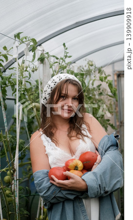 A seductive girl collects organic tomatoes in a greenhouse in the village, is engaged in farming. 139909918