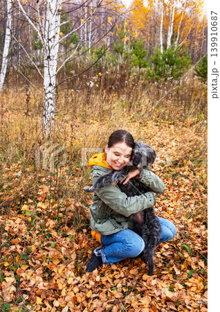 Woman hugging dog in an autumn forest. Young woman and pet together outdoors during fall season. Friendship between human and animal. Joyful leisure activity in nature among yellow leaves. Woman hugging dog in an autumn forest. Young woman and pet together outdoors during fall season. Friendship between human and animal. Joyful leisure activity in nature among yellow leaves. 139910687