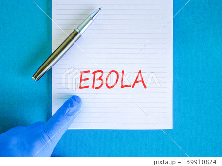 Ebola virus medical words symbol. Concept word Ebola on beautiful white note. Beautiful blue background. Doctor hand in blue medical glove. Black pen. Medical Ebola virus concept. Copy space. Ebola virus medical words symbol. Concept word Ebola on beautiful white note. Beautiful blue background. Doctor hand in blue medical glove. Black pen. Medical Ebola virus concept. Copy space. 139910824