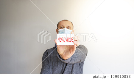Norovirus medical words symbol. Concept words Norovirus on beautiful white card. Beautiful white background. Beautiful handsome man patient in medical mask. Medical Norovirus concept. Copy space. Norovirus medical words symbol. Concept words Norovirus on beautiful white card. Beautiful white background. Beautiful handsome man patient in medical mask. Medical Norovirus concept. Copy space. 139910858