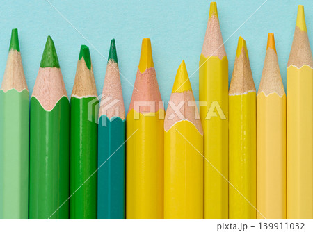 Close-up of a row of green and yellow wooden pencils on a blue background 139911032