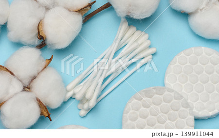 Cotton swabs, round discs and fluffy natural cotton bolls on blue background, top view Cotton swabs, round discs and fluffy natural cotton bolls on blue background, top view 139911044