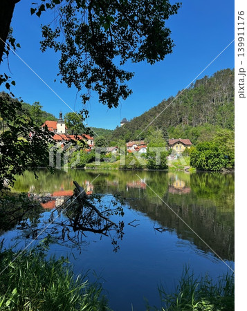 Scenic view of a tranquil river reflecting a small village surrounded by Scenic view of a tranquil river reflecting a small village surrounded by 139911176