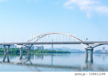 Beautiful yellow canola flowers (rapeseed) blooming along the Han River with Guri-Amsa Bridge in the background on a sunny spring afternoon Beautiful yellow canola flowers (rapeseed) blooming along the Han River with Guri-Amsa Bridge in the background on a sunny spring afternoon 139911199