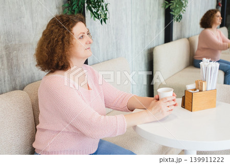 Middle-aged woman sitting in a cafe holding a coffee cup and looking thoughtful and relaxed 139911222