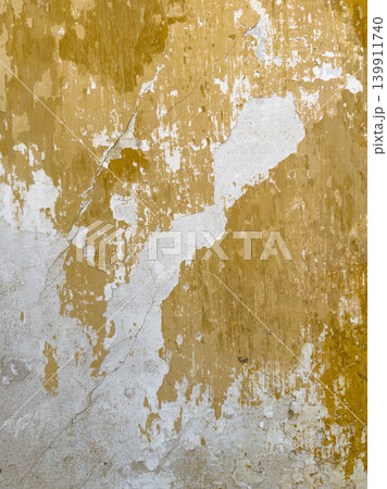Cracked wall surface with peeling mustard yellow paint layers revealing white plaster underneath for a rustic and authentic vintage architectural design 139911740