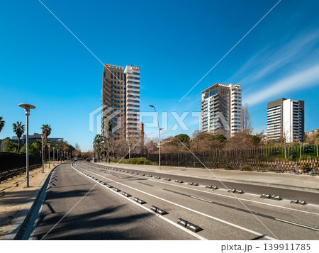 Urban landscape featuring modern skyscrapers along a clear road under a blue sky. Palm trees line the street, creating a vibrant city atmosphere. 139911785