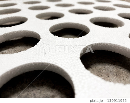 Closeup view of foam piece with multiple round holes cut. Concrete surface below, contrast to texture of foam. Crafts, projects or packing. Decorative for design Closeup view of foam piece with multiple round holes cut. Concrete surface below, contrast to texture of foam. Crafts, projects or packing. Decorative for design 139911953