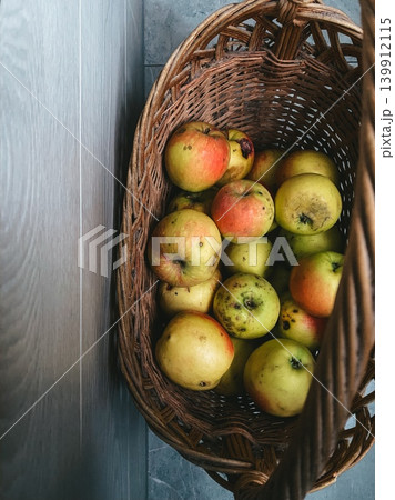 Wicker basket with assortment of fresh, ripe apples against wooden wall, top view. Bright yellow and red colors. Cozy atmosphere, harvest, natural organic food product Wicker basket with assortment of fresh, ripe apples against wooden wall, top view. Bright yellow and red colors. Cozy atmosphere, harvest, natural organic food product 139912115