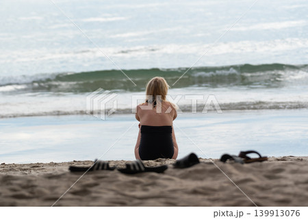 Woman sitting sandy beach looking at ocean waves calm moment travel relaxation seaside lifestyle natural light peaceful atmosphere horizon view Woman sitting sandy beach looking at ocean waves calm moment travel relaxation seaside lifestyle natural light peaceful atmosphere horizon view 139913076
