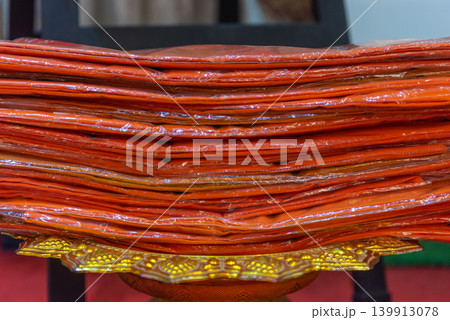 Stack of orange monk robes placed golden tray for buddhist ceremony offering tradition temple ritual fabric layers closeup cultural detail 139913078