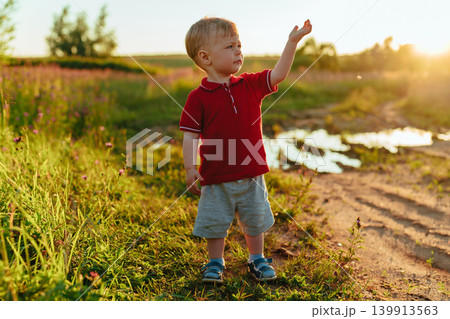 Two-year-old child standing in a field with his hand up Two-year-old child standing in a field with his hand up 139913563