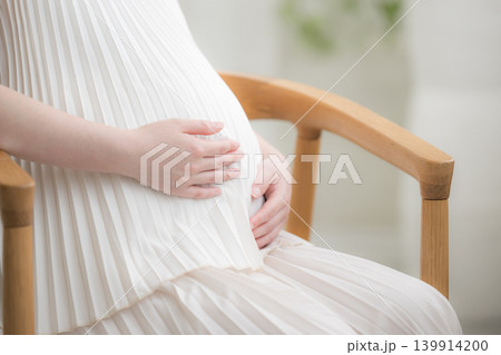笑顔でお腹に手を添える日本人女性の妊婦さん、マタニティライフスタイルイメージの笑顔で座る 顔無し手元 笑顔でお腹に手を添える日本人女性の妊婦さん、マタニティライフスタイルイメージの笑顔で座る 顔無し手元 139914200