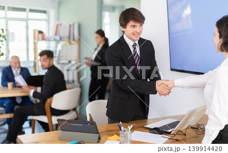 Young bank manager shaking hands with adult female client Young bank manager shaking hands with adult female client 139914420