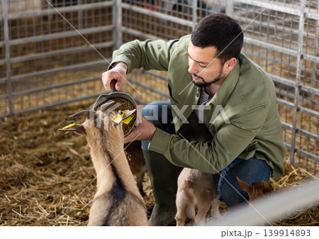 Positive male farmer taking care of goatlings Positive male farmer taking care of goatlings 139914893