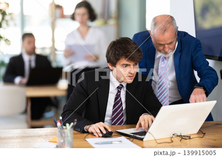 Elderly man helping young male colleague work on laptop 139915005