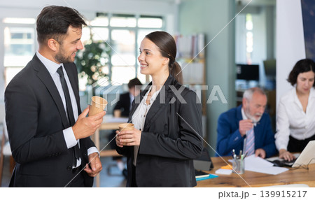 Young business woman and man co-worker employees drinking coffee and talking during break while working in office Young business woman and man co-worker employees drinking coffee and talking during break while working in office 139915217
