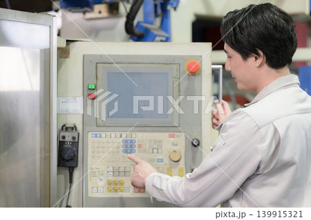 工場や製造現場で設備を操作する若手作業員と生産管理イメージ　パネルをタップする 139915321