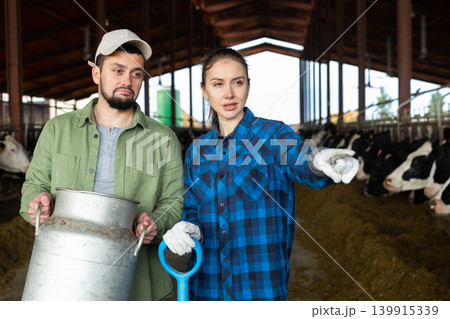 Man and woman farmers standing in cowshed and talking Man and woman farmers standing in cowshed and talking 139915339